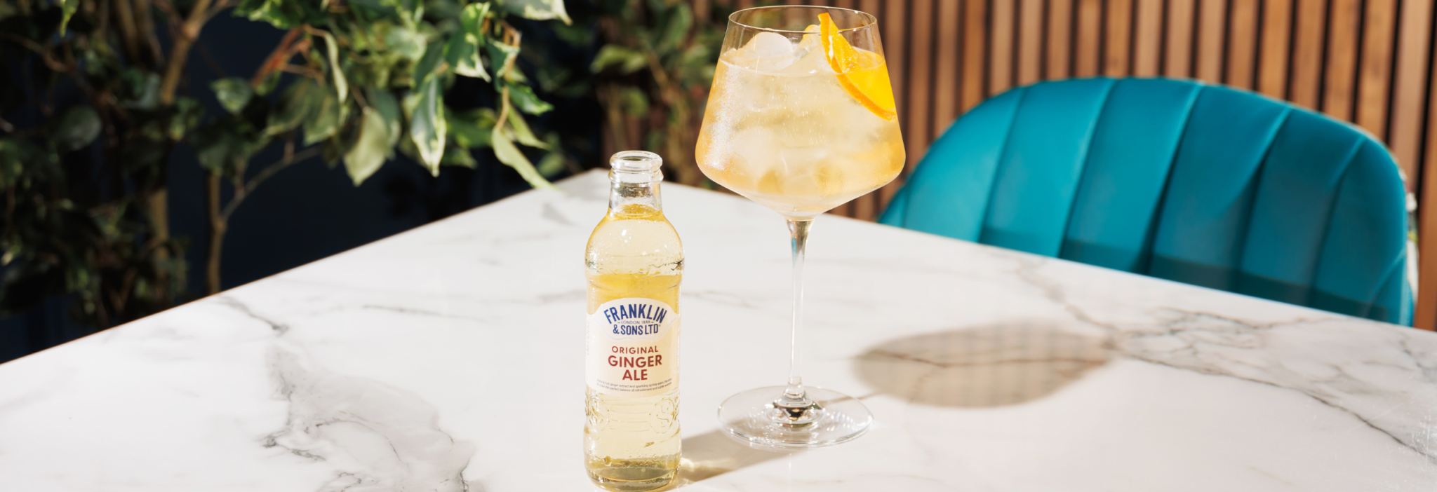 Original Ginger Ale next to a spritz cocktail in a wine glass with a orange peel slice as the garnish with a floral background | Franklin & Sons